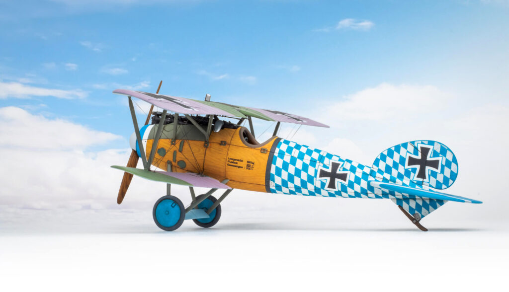 An albatros D.Va aircraft finished unnatural wood and blue and white chequers stands before a blue sky background